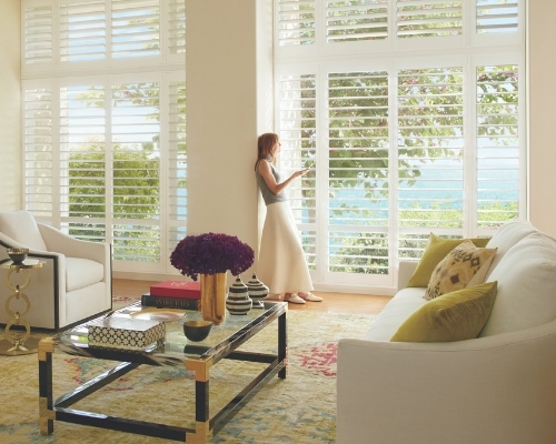 Woman standing in living room adjusting motorized shutters with PowerView® App